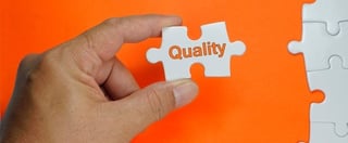 Hand holding jigsaw peice with the word 'quality' printed on the front